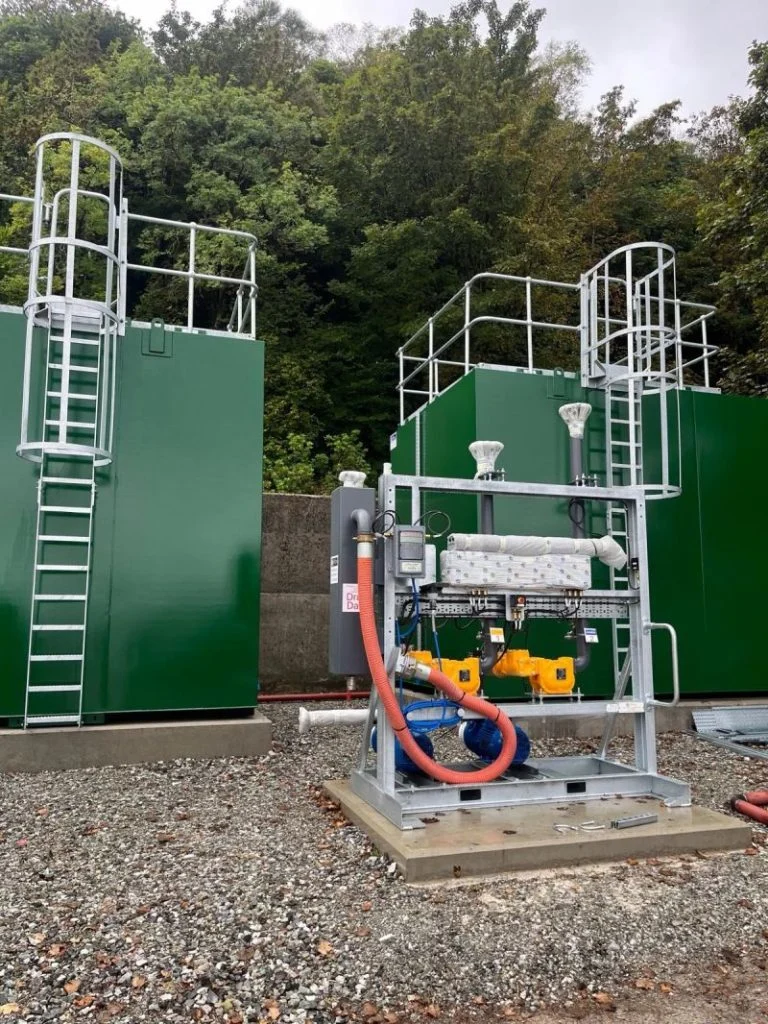 Loading skid with pumps and pipework beside large green cabinets